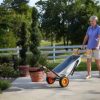 Women in blue outfit pushing aerocart wheelbarrow carrying large plant