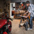 man using oscillating tool to sand down wood piece next to red bike