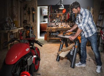 man using oscillating tool to sand down wood piece next to red bike