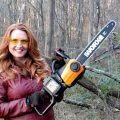 women holding chain saw in the woods next to tree