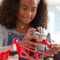girl using portable air brush to spray paint a craft red