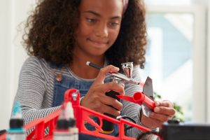 girl using portable air brush to spray paint a craft red