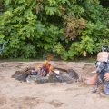 man, child, and dog sitting chair on sand next to fire