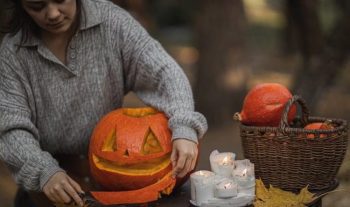 women holding the mouth of cut out pumpkin next to candles