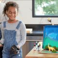 holding worx air brush and battery and charger next to sky painted box and dinosaurs