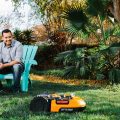 man sitting in yard watching Worx Landroid robotic mower auto mow the lawn