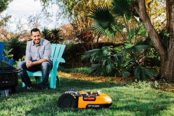 man sitting in yard watching Worx Landroid robotic mower auto mow the lawn