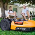 close up of Worx Landroid robotic lawn mower mowing lawn with man and woman sitting in the background