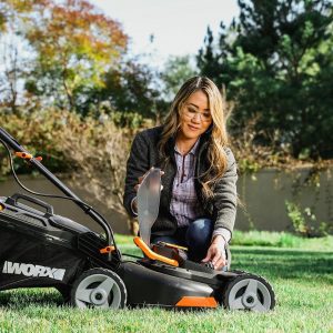 woman kneeling grass and placing battery into Worx cordless lawn mower