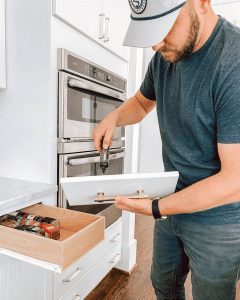 man in hat using electric drill to screw in handle of drawer