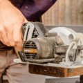 Man holding compact circular saw cutting edge of wood