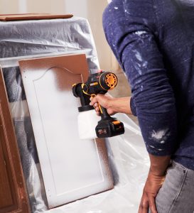 using paint sprayer to paint white color on to brown cabinet door