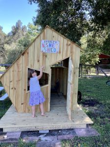 girl standing in front of wooden play house pointing at welcome sign