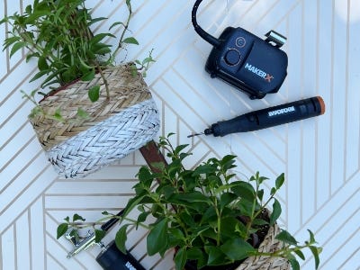 2 plants sitting inside basket next to rotart drill anad battery and charger