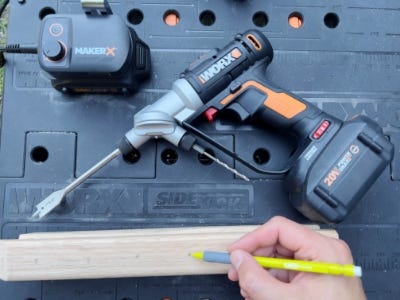 using pencil to write a wooden block next to drill on work table