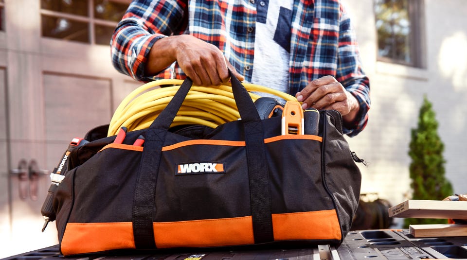 man in a plaid shirt putting a rolled up extension cord into the bag