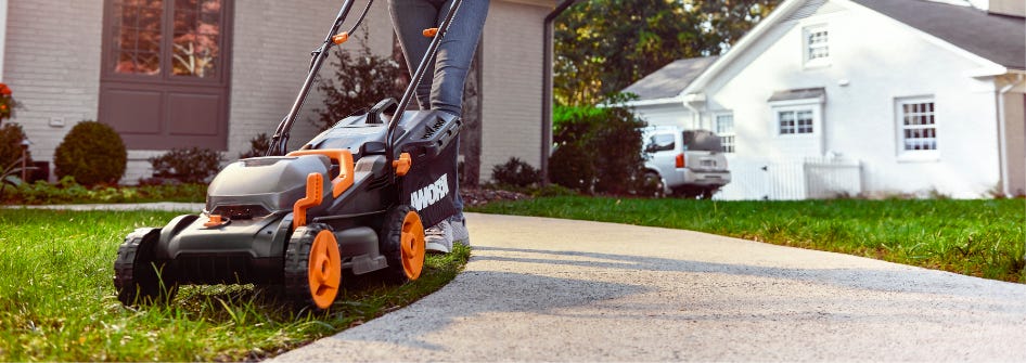 person using Worx cordless lawn mower to mow lawn next to cement walkway