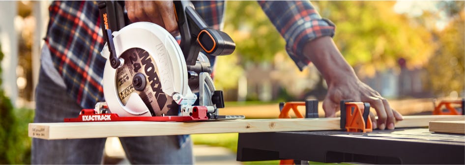 WORX Power Share ExacTrack 6-1/2" Circular Saw Man Cutting Wood Plank WORX Power Share ExacTrack 6-1/2" Circular Saw Man Cutting Wood Plank