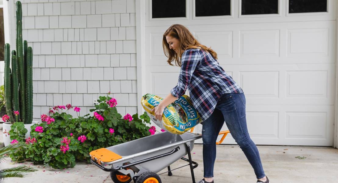 Lady adding soil bag into worx aerocart in front of flowers and garage door