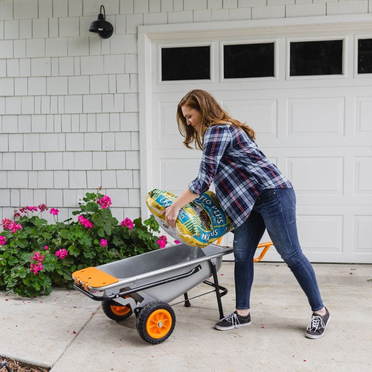 Lady adding soil bag into worx aerocart in front of flowers and garage door