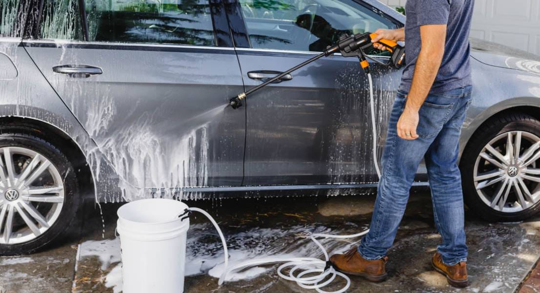 Worx hydroshot cleaning off side of grey car next to bucket of water