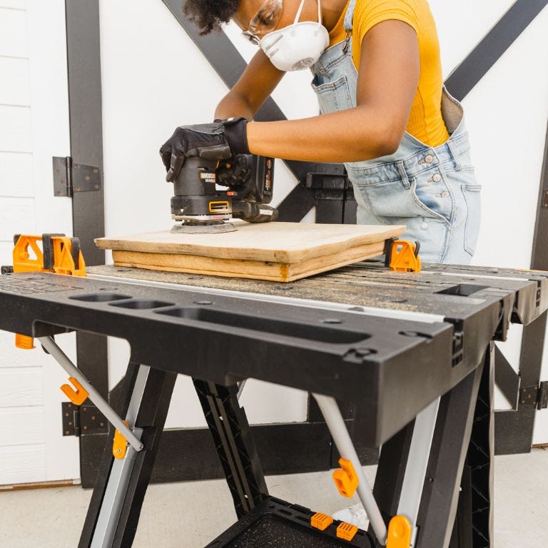 Lady sanding down wood on top of worx pegasus table