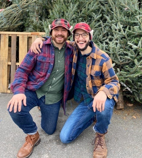 men in flannel shirts kneeling in front of fence and Christmas trees