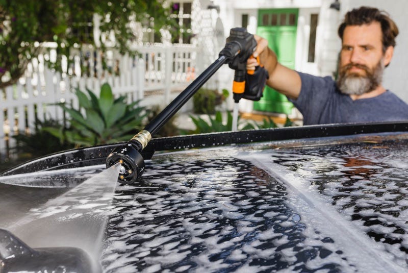 man using worx hydroshot portable power cleaner and soap to clean roof of car