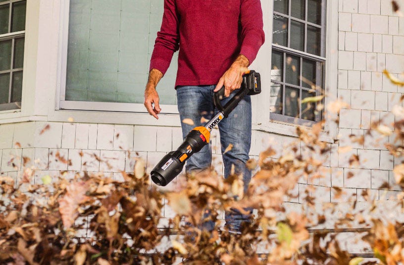 man holding bag of leaves with worx leafjet and leaf collection bag in driveway in front of brick house linking to worx leafjet product page