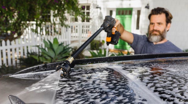 man using worx hydroshot portable power cleaner and soap to clean roof of car