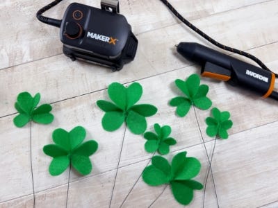 felt hearts glue onto sticks to make the shapes of clovers on a table next to the makerx glue gun and hub