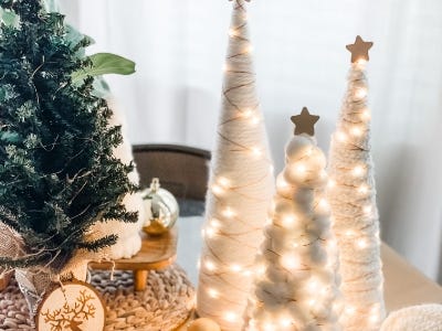 three yarn trees with lights wrapped around them in front of greenery