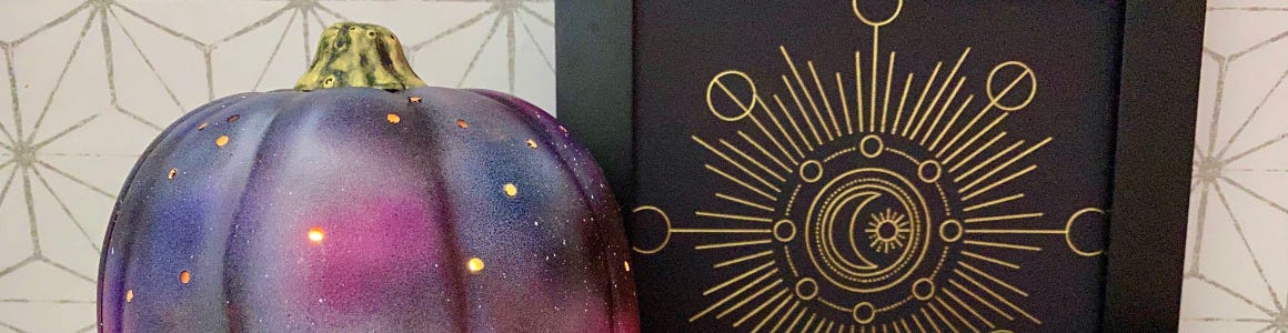 Galaxy printed plastic pumpkin on a table next to Halloween artwork with a gold moon on a black background