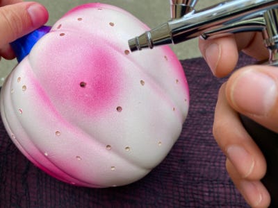 Pink color air brush paint being painted on to white pumpkin
