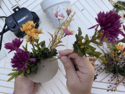 poking fake plants into cardboard circle