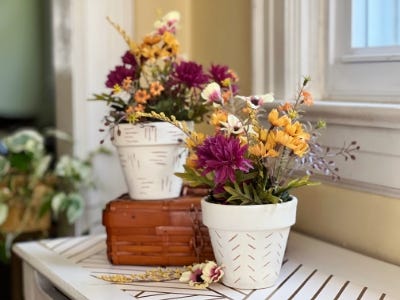 two hand etched pots and one is on book on wooden table with flowers laying down in front of