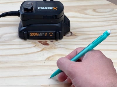 person holding a pencil and the makerx hub on top of the wooden round