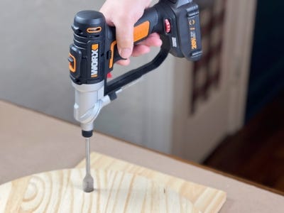 person using the worx switchdriver to drill a hole in the wooden round