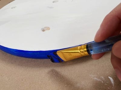 person painting the edge of the wooden round blue