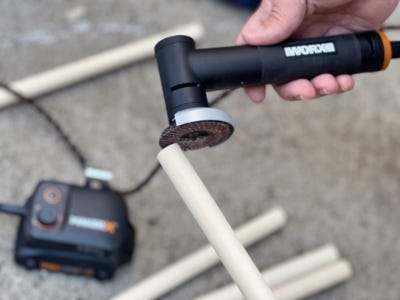 person using the rotary tool to sand the wooden dowel