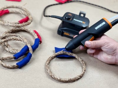 person using the hot glue gun on the rope with the makerx hub in the background