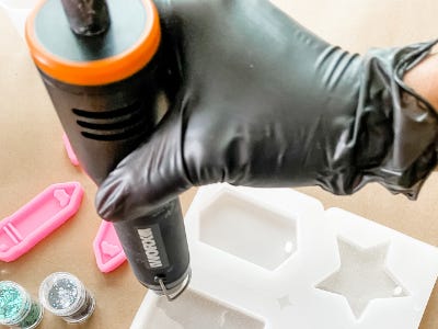 wearing black glove pouring a thin amount of resin into plastic mold