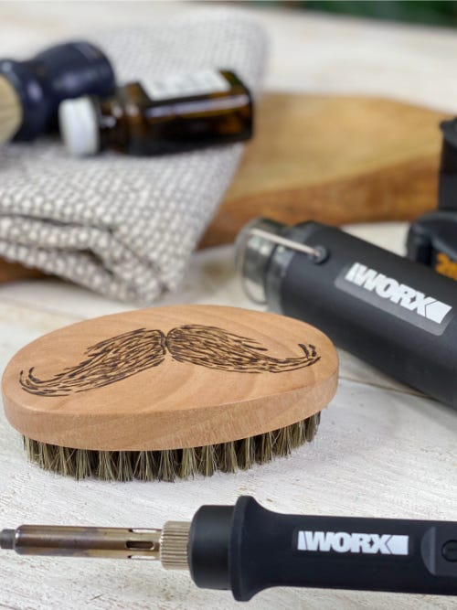beard brush with wood burned mustache design next to makerx heat gun