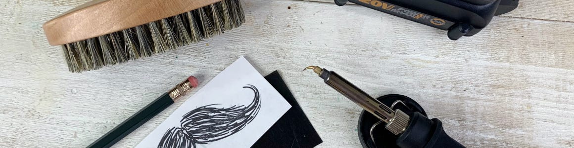 Beard Brush Hero Image wood and metal crafter laying next to mustache printing and beard brush