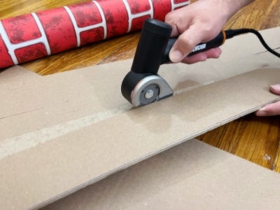 rotary cutter cutting down the middle of cardboard next to red paper