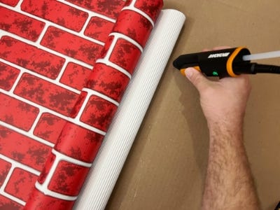 using hot glue gun to glue red and brick paper to cardboard