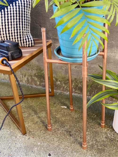 copper pipe planter holding a green fern plant in a blue pot