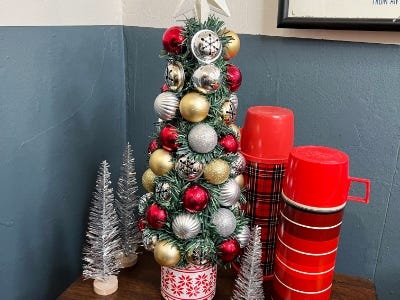 Top of Oranament tree on table next to smaller silver trees and two red cups