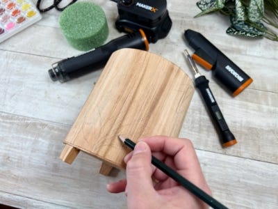 image of a person sketching a design on the wooden pot with the MAKERX tools in the background