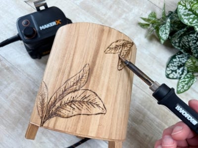 image of the the person using the wood and metal crafter tool to complete etching the design into the wooden pot